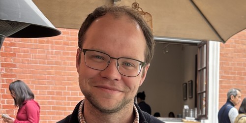 A white man with glasses and brown hair smiles.